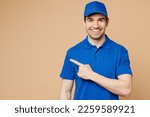 Small photo of Happy delivery guy employee man wearing blue cap t-shirt uniform workwear work as dealer courier pointing index finger aside indicate on area isolated on plain light beige background. Service concept