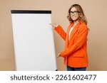 Young smling successful employee business woman corporate lawyer 30s wears classic formal orange suit glasses work in office show flipchart marker board graph isolated on plain beige background studio