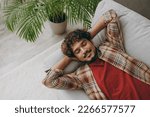 Top with young Indian man wearing casual clothes close eyes take nap sleep lay down on grey sofa couch stay at home hotel flat rest relax spend free spare time in living room indoor. Lounge concept