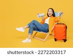 Young excited woman wear summer clothes sit in deckchair scream in megaphone isolated on plain yellow background. Tourist travel abroad in free spare time rest getaway. Air flight trip journey concept