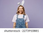 Small photo of Young smiling satisfied woman wear white casual clothes bunny rabbit ears looking camera wink blink eye isolated on plain pastel light purple background studio portrait. Lifestyle Happy Easter concept