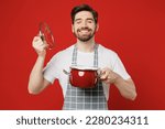 Small photo of Young fun male housewife housekeeper chef cook baker man wear grey apron hold in hand pot lid open saucepan sniff scent enjoy close eyes isolated on plain red background studio. Cooking food concept