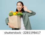 Small photo of Young woman wear casual clothes hold brown paper bag with food products try hear you overhear listen intently isolated on plain blue background studio portrait Delivery service from shop or restaurant
