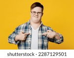 Small photo of Young smiling cheerful man with down syndrome wear glasses casual clothes look camera point index finger on himself isolated on pastel plain yellow color background. Genetic disease world day concept