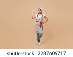Small photo of Full body satisfied happy young housewife housekeeper chef baker latin woman wear apron toque hat show ok okay gesture stand akimbo isolated on plain pastel light beige background. Cook food concept