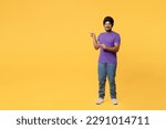 Small photo of Full body smiling devotee Sikh Indian man ties his traditional turban dastar wear purple t-shirt point index finger aside on workspace area mock up isolated on plain yellow background studio portrait