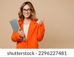 Small photo of Young employee IT business woman corporate lawyer 30s wear classic formal orange suit glasses work in office hold closed laptop pc computer point finger aside isolated on plain beige background studio
