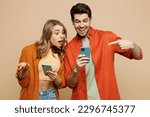 Small photo of Young happy confused couple two friends family man woman wear casual clothes hold use point finger on mobile cell phone together isolated on pastel plain light beige color background studio portrait