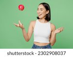 Small photo of Young fun vegetarian woman wear white clothe hold in hand toss up ripe red apple playing isolated on plain pastel light green background. Proper nutrition healthy fast food unhealthy choice concept