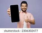 Small photo of Young Indian man wears pink shirt white t-shirt casual clothes hold in hand use close up mobile cell phone with blank screen workspace show thumb up isolated on plain pastel light purple background