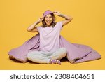 Small photo of Full body young happy woman wears purple pyjamas jam take off sleep eye mask rest relax at home sit with blanket duvet hold pillow wake up wink isolated on plain yellow background. Night nap concept