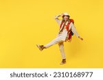Full body fun young woman carry bag with stuff mat touch hat raise up leg isolated on plain yellow background. Tourist leads active lifestyle walk on spare time. Hiking trek rest travel trip concept