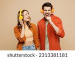 Small photo of Young fun couple two friends family man woman wear casual clothes headphones listen music sing song in microphone looking camera together isolated on pastel plain light beige color background studio
