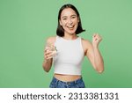 Small photo of Young woman wear white clothes hold drink clear fresh pure still water from glass do winner gesture isolated on plain pastel light green background. Proper nutrition healthy fast food choice concept