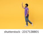 Small photo of Full body fun side view smiling cheerful devotee Sikh Indian man ties his traditional turban dastar wear purple t-shirt walking going waving hand isolated on plain yellow background studio portrait