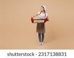 Small photo of Full body young housewife housekeeper chef baker latin woman wear striped apron toque hat woman hold baking sheet with chocolate cookies look aside isolated on plain beige background Cook food concept