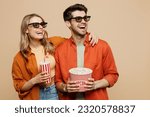 Small photo of Young fun couple two friends family man woman in 3d glasses wear casual clothes watch movie film hold bucket of popcorn cup of soda pop in cinema look aside isolated on plain beige background studio