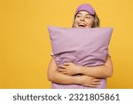 Fun young woman she wears purple pyjamas jam sleep eye mask rest relax at home hold pillow look aside on workspace area isolated on plain yellow background studio portrait Good mood night nap concept