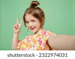 Close up happy little child kid girl 6-7 years old wear casual clothes have fun do selfie shot pov on mobile cell phone show v-sign isolated on plain green background. Mother's Day love family concept