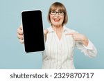 Employee business woman 50s wears white classic suit glasses formal clothes hold use point on blank screen area mobile cell phone isolated on plain pastel blue background. Achievement career concept