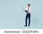 Full body young employee IT business man corporate lawyer wears classic formal shirt tie work in office hold clipboard with paper account documents point pen aside isolated on plain blue background