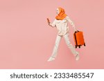 Traveler arabian woman wear orange abaya hijab hold mobile phone bag isolated on plain pink background Tourist travel abroad in free time rest getaway Air flight trip, uae middle eastern islam concept