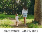Full body back view young woman in white clothes have fun with cute child baby girl 5-6 year old walk go along forest path Mommy play rest with little kid daughter outdoor together Love family concept