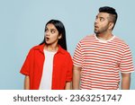 Young shocked surprised astonished couple two friends family Indian man woman wearing red casual clothes t-shirts look aside on area together isolated on pastel plain light blue cyan color background