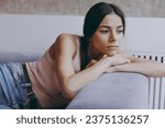 Small photo of Unnerved sad worried minded young latin woman 20s in casual clothes sit lay on sofa think plan hands folded under head look aside spend time in living room home in own house. People emotions concept