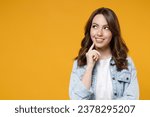 Small photo of Young smiling dreamful wistful woman in stylish casual denim shirt white t-shirt show prop up chin look aside up empty space deep thinking creative person isolated on yellow background studio portrait