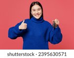 Young happy woman of Asian ethnicity she wear blue sweater casual clothes hold key fob keyless system show thumb up isolated on plain pastel light pink background studio portrait. Lifestyle concept