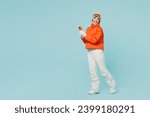 Full body happy young skier woman wear warm padded windbreaker jacket hat ski goggles mask use mobile cell phone travel rest spend weekend winter season in mountains isolated on plain blue background