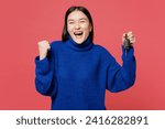 Young fun woman of Asian ethnicity she wear blue sweater casual clothes hold key fob keyless system do winner gesture isolated on plain pastel light pink background studio portrait. Lifestyle concept
