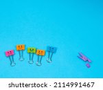 Small photo of Funny multicolored smile metal binder clip or paper clip deride or laugh wooden violet clothespin with fracture leg on blue background. Copy space for text. Different, stand out of crowd concept