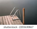 Old wooden pier with ladders to a lake. Autumn sunrise and foggy lake.