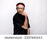 A portrait of an Asian man celebrating Independence Day, wearing a black shirt and a red and white headband, showing a strong gesture by lifting his arms and flexing his muscles. Isolated with a white