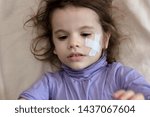 Small photo of Little kid girl after accident laying down with adhesive palter on face