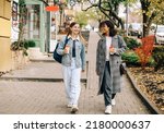 Small photo of Two happy carefree multiracial girlfriends walking city street with take away coffee, talking and sharing life stories, multiethnic female best friends enjoying autumn walk outdoors. Womens friendship