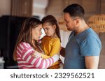 Small photo of Young parents comfort their cute daughter. Beautiful woman hugs and talks to little girl in living room at home. Dad and mom take care of their child. Tender moment family support and understanding.