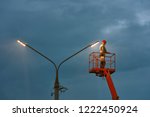 Municipal worker with helmet and safety protective equipment installs new diode lights. Worker in lift bucket repair light pole. Modernization of street lamps. Technician on aerial device. Night duty