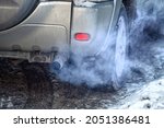 Small photo of Blue exhaust smoke. Car engine smoking. Smoking exhaust pipe, closeup. Car with gasoline or diesel engine. Engine warming up at idle in winter season