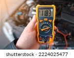 Man testing car electrical system including battery, alternator for winter. Check car battery using voltmeter. Man use multimeter with voltage range measurement to check up voltage level. Low voltage