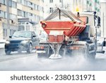 Small photo of Snow plow truck spreading salt on asphalt road. Truck salting road and highway during blizzard in winter season. Orange snow plow truck in action. Utility vehicle spreading deicing rock salt