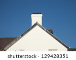 A white painted gable end with plastic barge boards a chimney and pots with a slate roof against a blue sky.