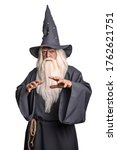 Small photo of A stern grey-haired bearded wizard in a gray cassock and a cap is practicing sorcery and doing magic against a white insulating background.