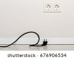 Small photo of Black power cord cable unplugged with european wall outlet on white plaster wall with copy space