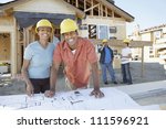 Portrait of happy African American couple at construction site with builders standing background