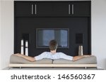 Rear view of young man watching television while sitting on couch in living room