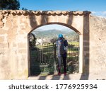 Woman hiker or backpacker looking into private almond orchard through ols stony entrance gate. 
