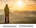 Woman stands alone on the peak of rock. Hiker watching to autumn Sun at horizon . Beautiful moment the miracle of nature. Colorful mist in valley. Man hike. Person silhouette stand